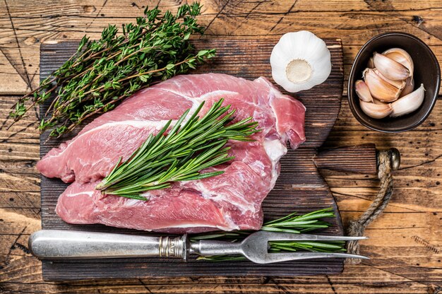 木製の肉屋のボードに食材とスパイスを添えた新鮮な生の豚肩肉。木製の背景。上面図。