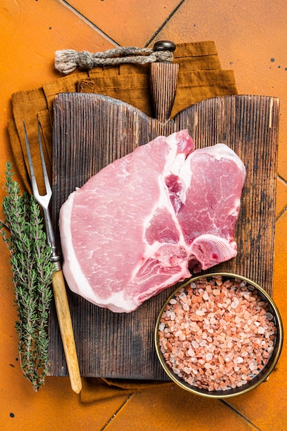 Foto bistecca di carne fresca di maiale crudo su un tavolo da taglio sfondo arancione vista superiore