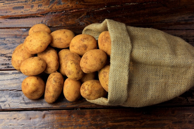 Fresh and raw potatoes harvested from plantation and placed in a rustic bag on wooden table