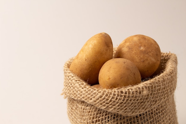 Foto patate fresche e crude in un sacco rustico isolato su bianco