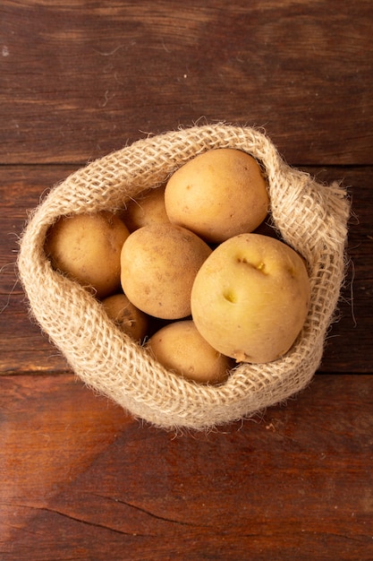 Свежий и сырой картофель в деревенском мешке на деревянный стол