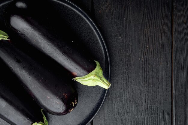 Photo fresh raw purple eggplant set, on black wooden table background, top view flat lay, with copy space for text