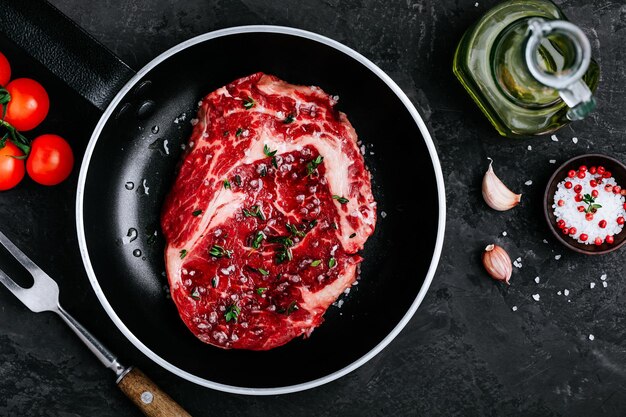 Fresh Raw Rib Eye Steak in frying pan on dark stone background prepared for cooking barbeque grill Top view copy space