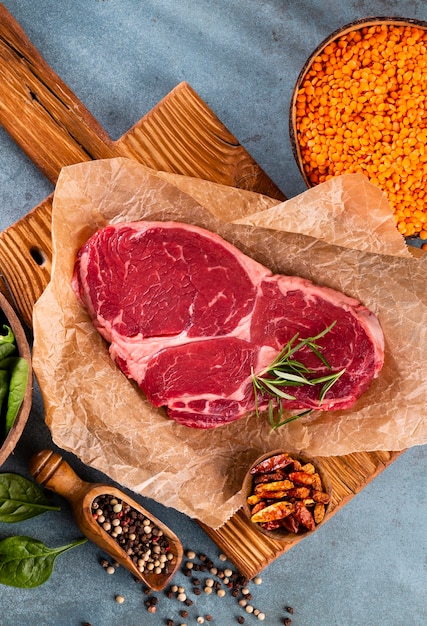 Fresh raw rib-eye steak on wooden cutting board, with spinach, lentils and rosmary in a rustic style.