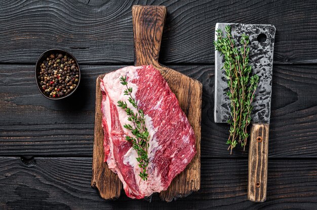 Fresh raw round roast beef meat cut on a butcher cutting board\
with cleaver. black wooden