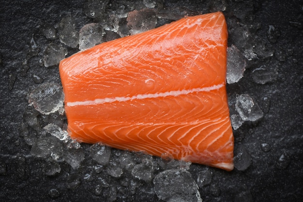 Fresh raw salmon fish steak on ice and dark stone table