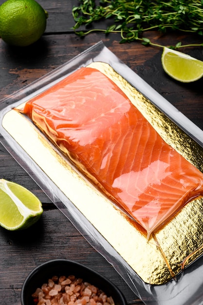 Fresh raw salmon fish steak in vacuum pack set, with herbs, on old dark  wooden table background