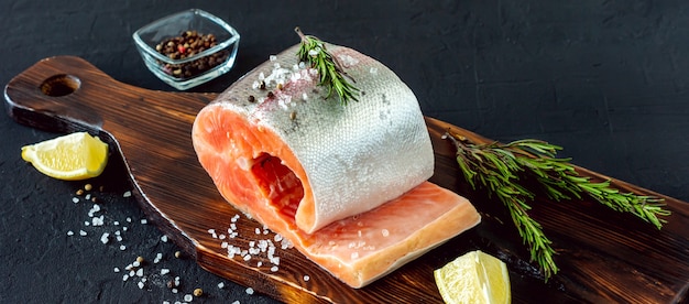 Fresh raw salmon steak with lemon, hearbs and spices on cutting board.