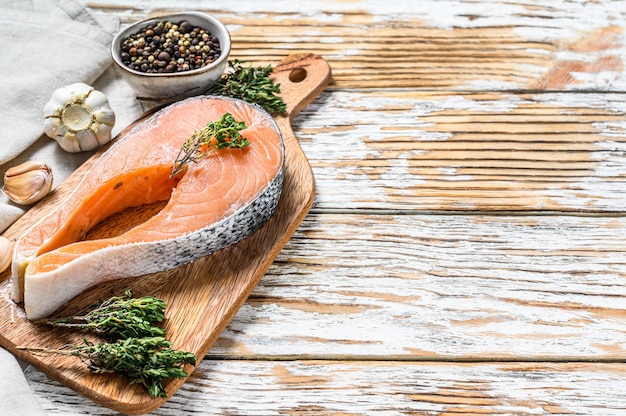 Fresh raw salmon steak with pepper and thyme. White wooden space. Top view. Copy space