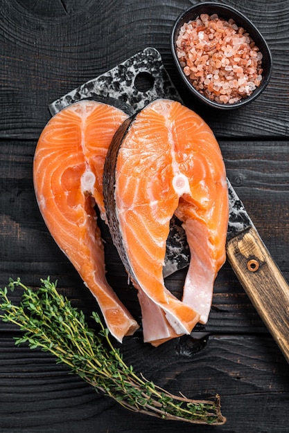 Bistecche di salmone crudo fresco sulla mannaia del macellaio. fondo in legno nero. vista dall'alto.