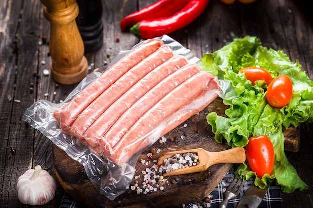 fresh raw sausages, in plastic packaging, on kitchen cutout board  table on black background