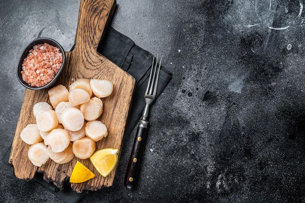 Fresh Raw scallops on a wooden board with sea salt Black background Top view Copy space