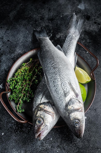 Fresh Raw Sea Bass Labrax fish with herbs and lime Black background Top view