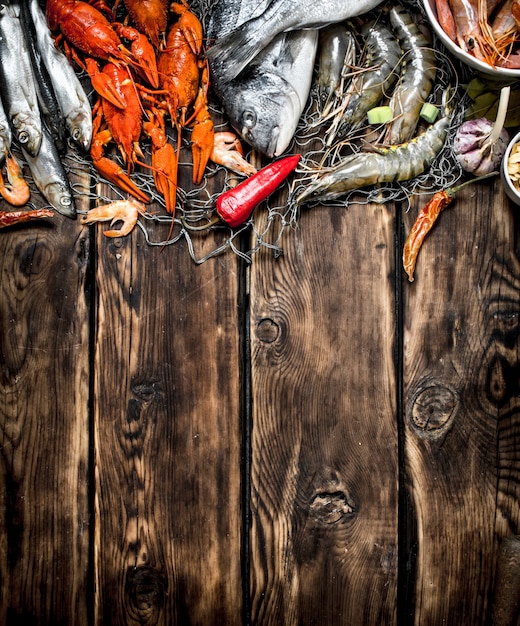 Свежие сырые морепродукты. Разнообразие морепродуктов на рыболовной сети. На деревянном столе.