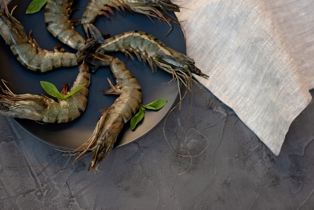 Fresh raw shrimp prawns on a black plate. Healthy seafood is a source of protein. Flat lay. Copy space.