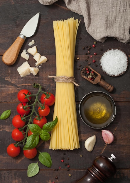 Fresh raw spaghetti pasta with cherry tomatoes and basil garlic and oil with parmesan cheese and salt and pepper on wooden backgroundTop view