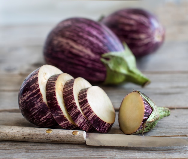 Fresh Raw striped eggplants and slices with knife on old wooden table, close up