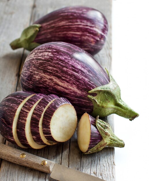 Fresh Raw striped eggplants and slices with knife  on a wooden table close up