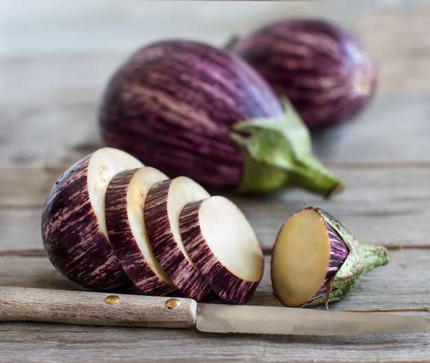 Fresh Raw striped eggplants and slices with knife on wooden table close up