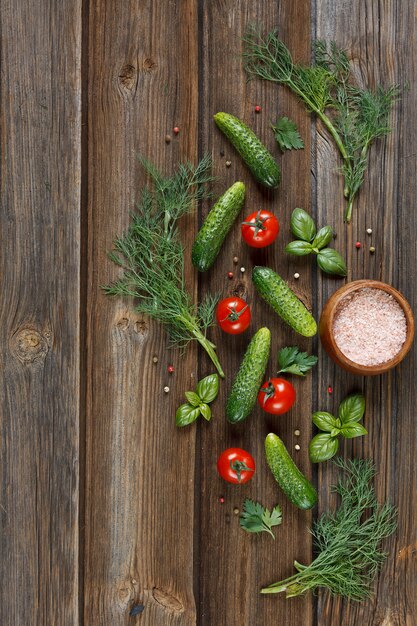 Fresh raw tomatoes, cucumbers and seasonal greens. Top view, a rough plan on a vintage wooden table