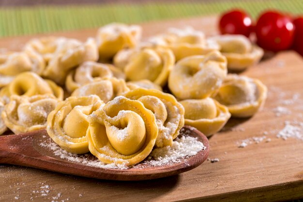 Fresh raw tortellini pasta, with cherry tomatoes over wood with wheat flour.