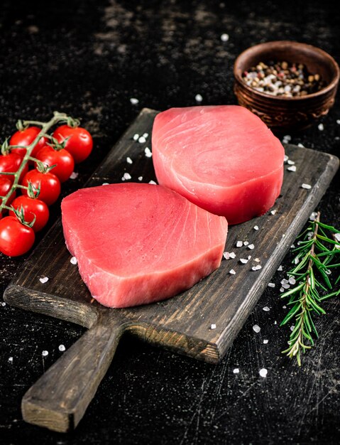 fresh raw tuna on a cutting board with tomatoes spices and rosemary