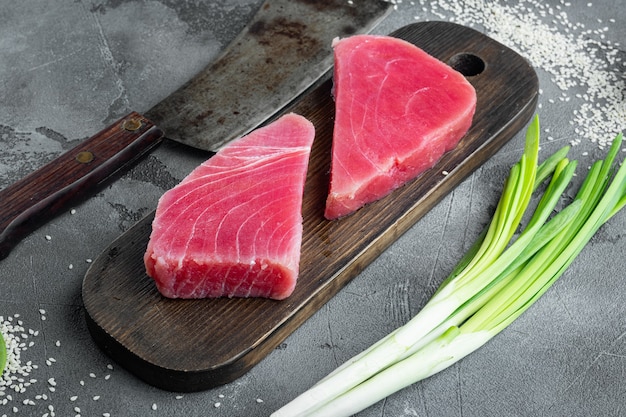 Fresh raw tuna fish steak with green pea, sesame and spring\
onions set, on wooden cutting board, and old butcher cleaver knife,\
on gray stone