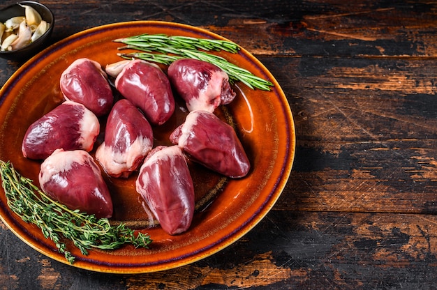 Fresh Raw turkey hearts offal giblets with  thyme and rosemary. Dark wooden background. Top view. Copy space.