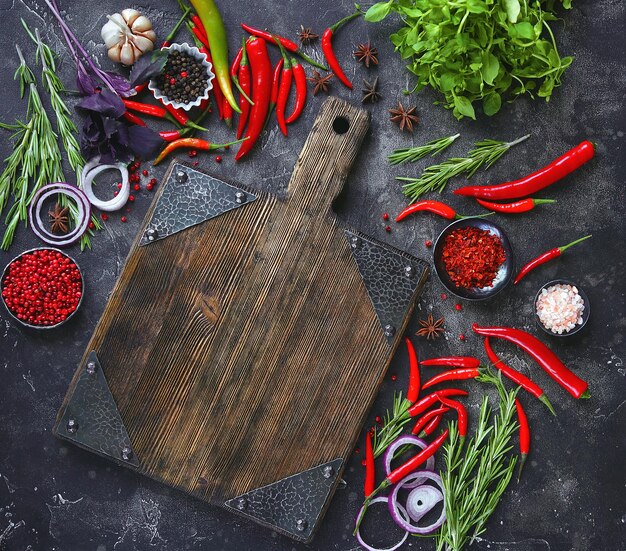 Fresh raw vegetables and empty cutting board on dark background