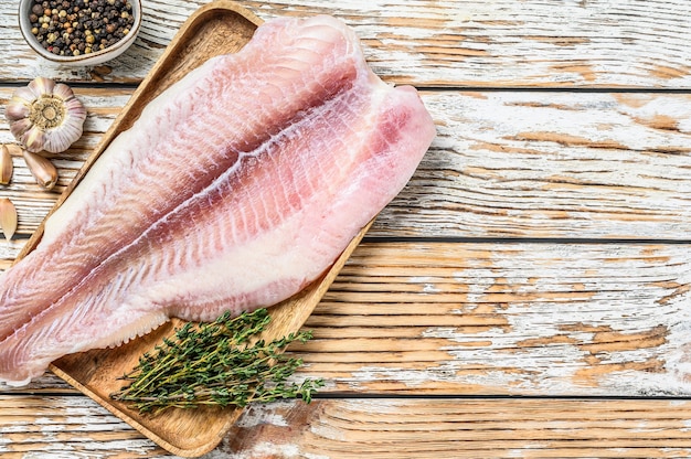 Pesce gatto di filetto di pesce bianco crudo fresco con spezie. fondo in legno bianco