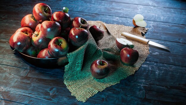 Fresh red apples in bowl with half apple and knife on fabric on wood