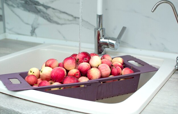 台所の流し台にある新鮮な赤いリンゴ、クローズアップ。ザルに入れて、流水で洗ったリンゴ。
