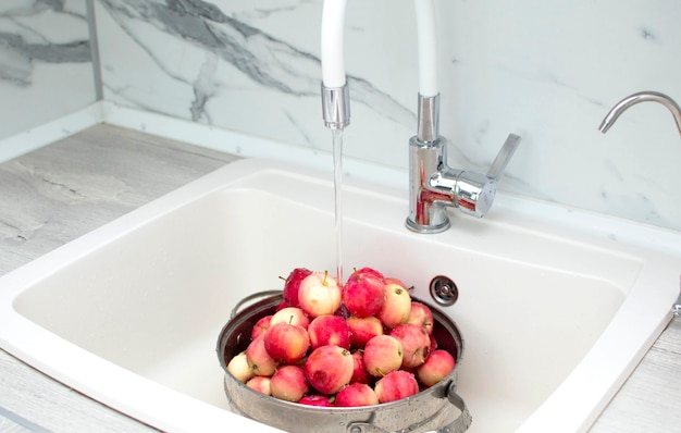 Fresh red apples in the kitchen sink, close-up. Apples in a colander, washed under running water.