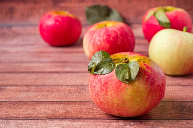 Fresh red apples with green leaves on a Dark wooden surface.