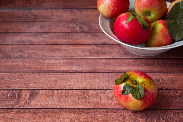 Fresh red apples with green leaves on a Dark wooden surface.