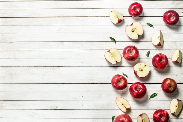 Fresh red apples with leaves on white wooden table.