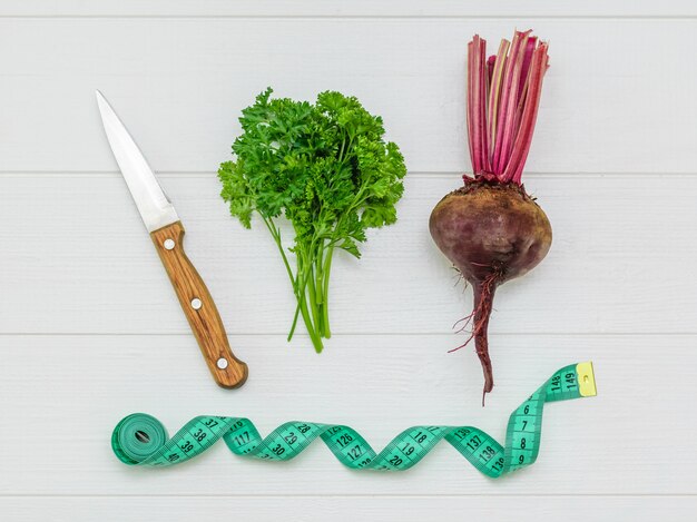 Fresh red beetroot with a knife and a bunch of parsley and measuring tape on a white wooden table