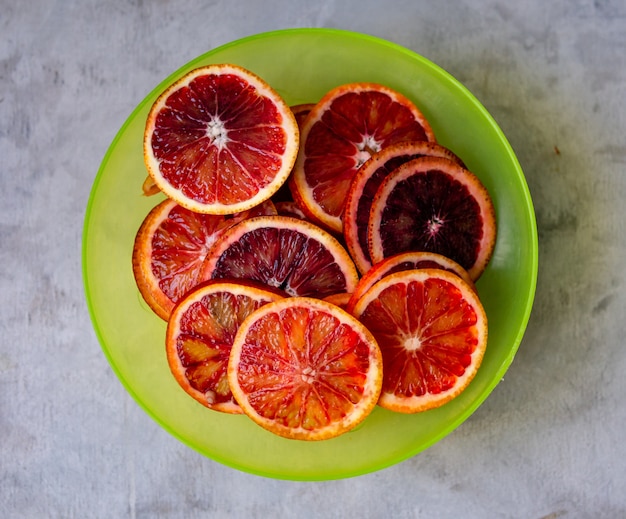 Fresh red blood oranges with slices in green plate on a gray background. Top View, selective focus.