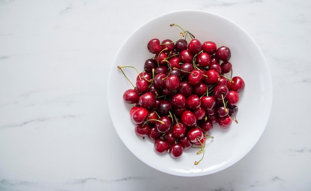 Fresh red cherries fruit on a white plate on a white surface