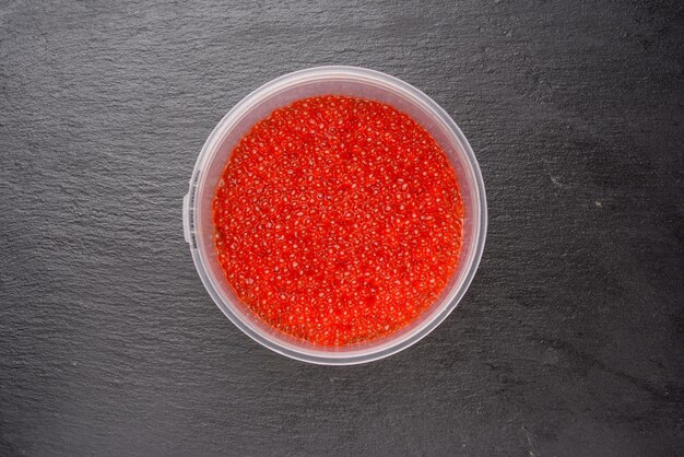 Fresh red chum salmon caviar in a plastic plate on a black background top view