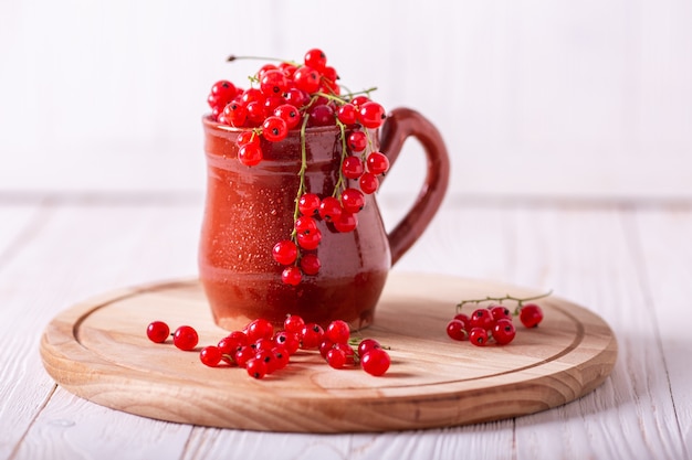 Fresh red currant in a ceramic cup on a white wooden background