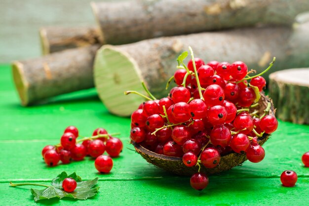 Fresh red currants in a bowl on a green wooden table. Close-up