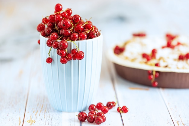 Fresh red currants in light blue cup on light wooden table.