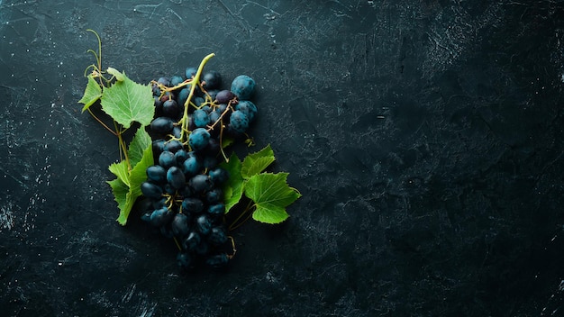 Fresh red grapes with leaves on a black stone table. Top view. Free space for your text.