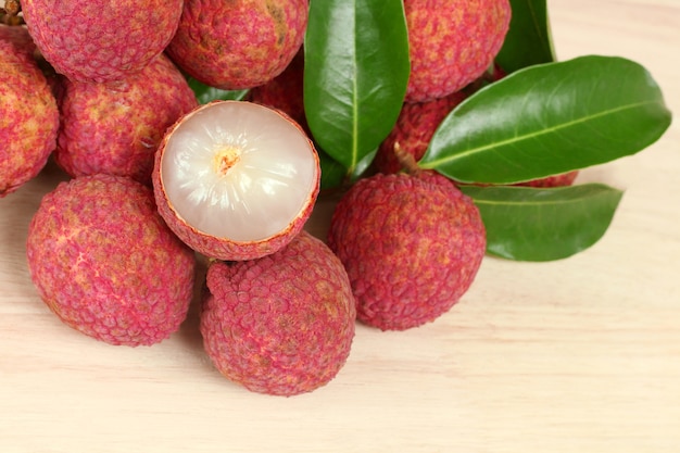 Fresh red lychee and peeled with leaves on wooden background with copy space.