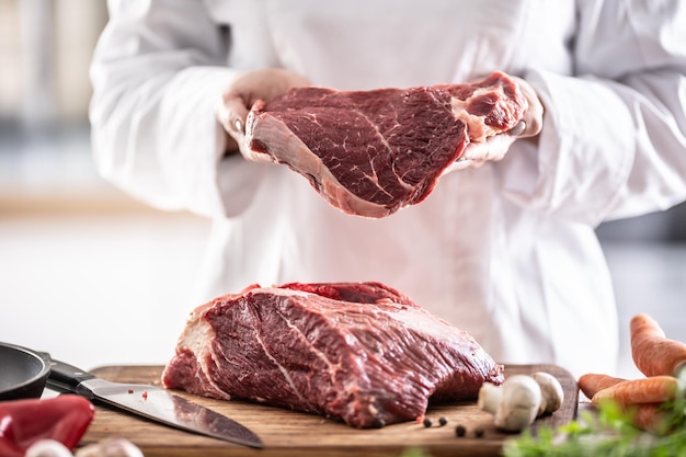 Fresh red meat cut in hands of a chef with chunk of meat on a wooden board.