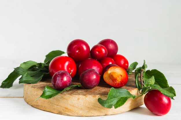 Photo fresh red plum with leaves on a wooden light background