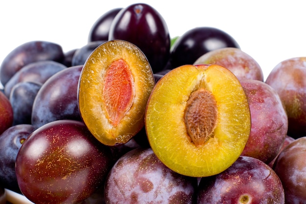 Fresh red plums with one sliced open to reveal the succulent yellow flesh and pip, over white