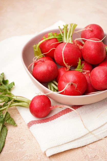 Fresh red radishes in a ceramic bowl over beige surface Closeup