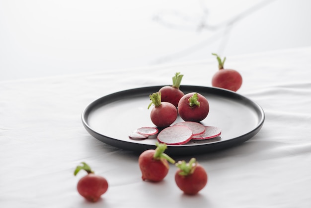 Fresh red radishes with stem and roots in a black dish on table